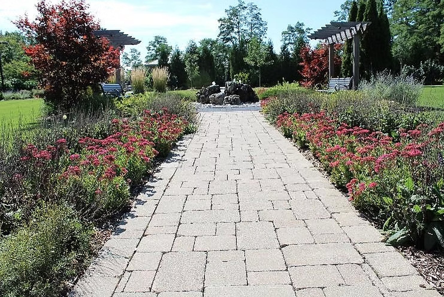 A stone pathway through deep perennial borders leading to a pergola and water feature