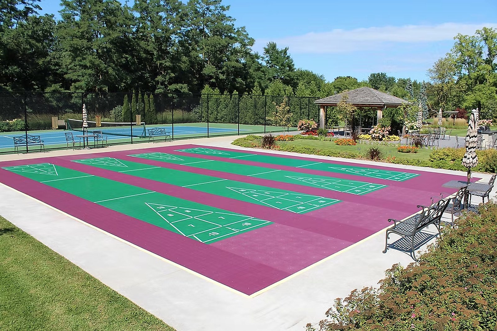 A bank of six shuffleboard courts in green and magenta, beside the tennis court and gazebo